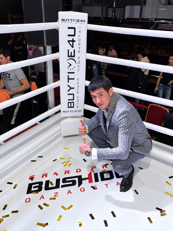Представитель BUYTIME4U стоит на ринге рядом с вертикальным баннером компании